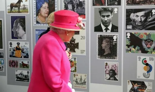 Королева Елизавета смотрит на выставку марок во время посещения отделения Королевской почты в честь 500-летия почтовой службы в 2016 году